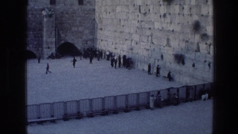 1976 8mm view of the Wailing Wall in Jerusalem with visitors and worshippers gathered near the stone wall.