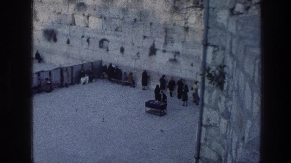 High-angle 1976 Jerusalem footage showing worshippers and visitors near the Wailing Wall, with a small table in the courtyard.