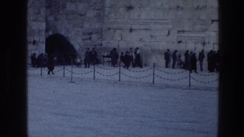 1976 8mm view of visitors gathered along the Western Wall in Jerusalem, with an arched opening and chains in the foreground.