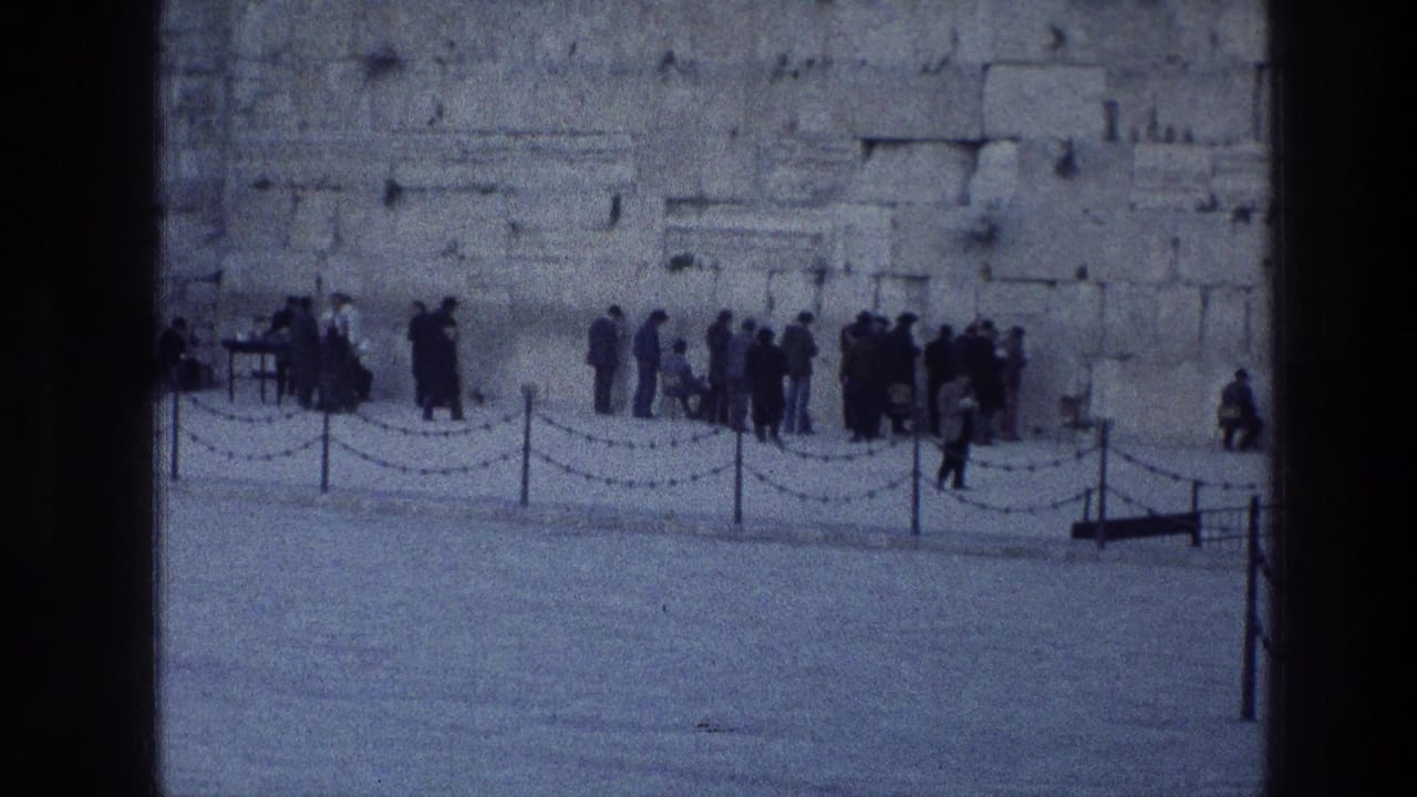 Visitors stand in small clusters at the Western Wall in Jerusalem, filmed from a distance on blue-tinted 8mm stock.