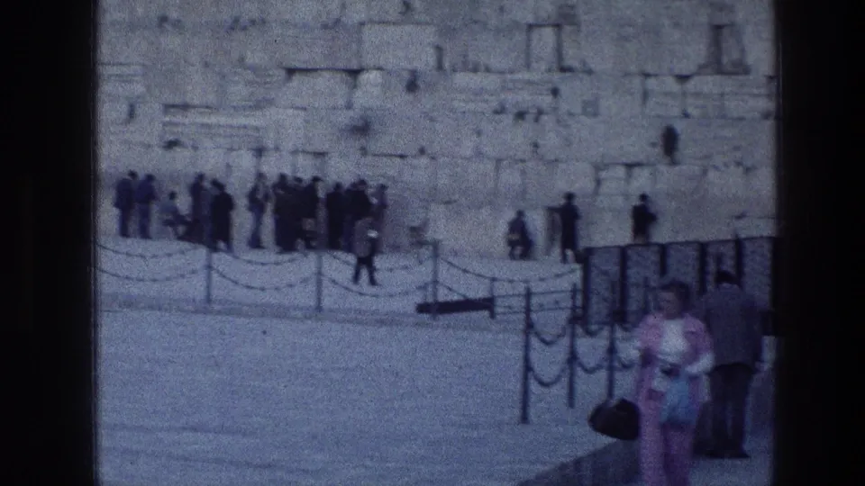 Western Wall visitors appear in the background while two closer figures cross the lower frame in 1976 Jerusalem home-movie footage.