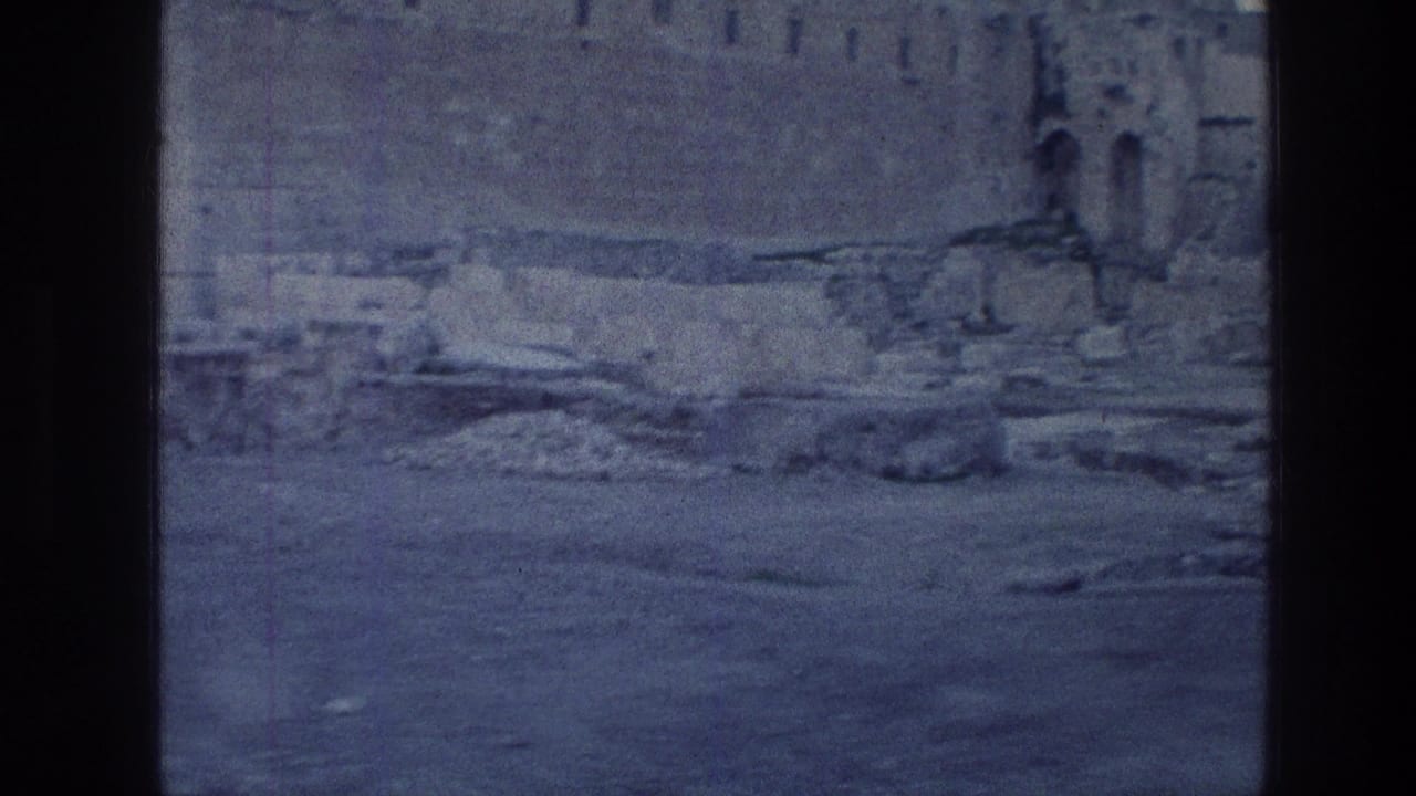 Vintage 8mm frame of the Jerusalem Wailing Wall area with rough stone courses, scattered rubble, and a cool blue daylight tint.