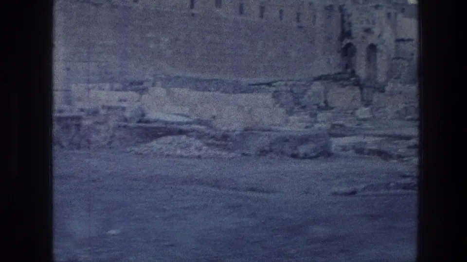 Vintage 8mm frame of the Jerusalem Wailing Wall area with rough stone courses, scattered rubble, and a cool blue daylight tint.