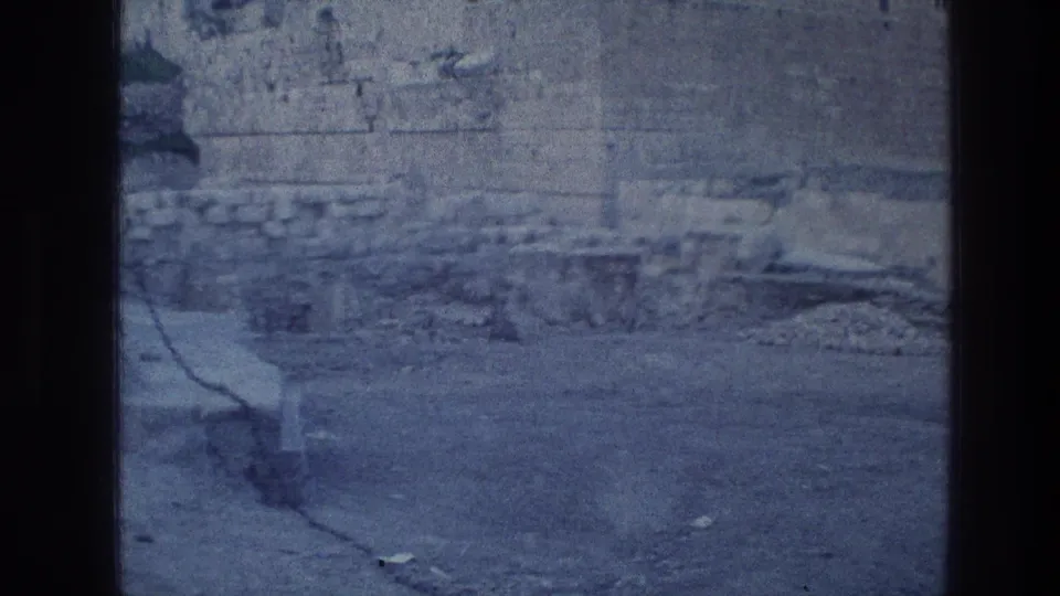 Final 8mm frame of the Jerusalem Wailing Wall area, with weathered stone masonry, rubble, and no visible people or signs.