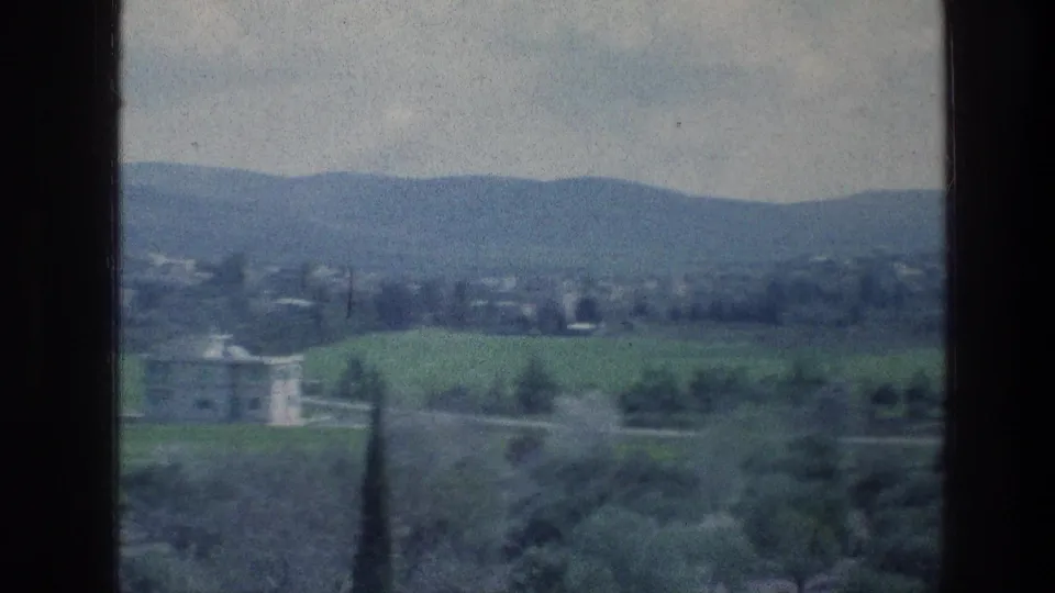 Soft blue-green 8mm view of the stated Jerusalem-area countryside, showing fields, trees, a pale villa-like structure, and low hills.