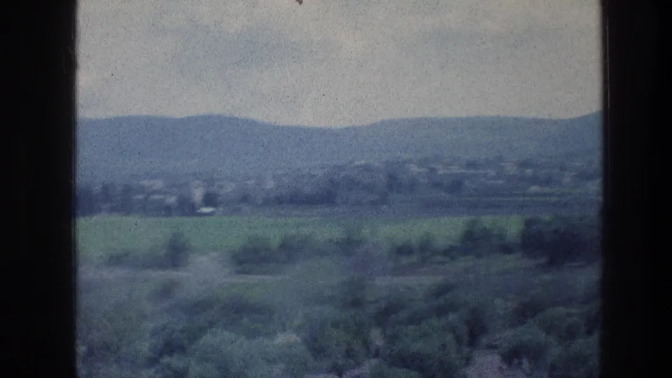 End frame of the 1976 8mm countryside view, with green fields, foreground trees, and distant hills in soft focus.