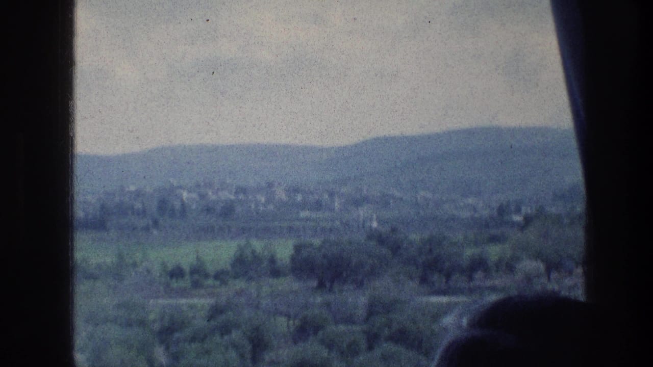 1976 8mm travel frame near Jerusalem with a green valley, low hills, distant structures, and dark window-like foreground edges.