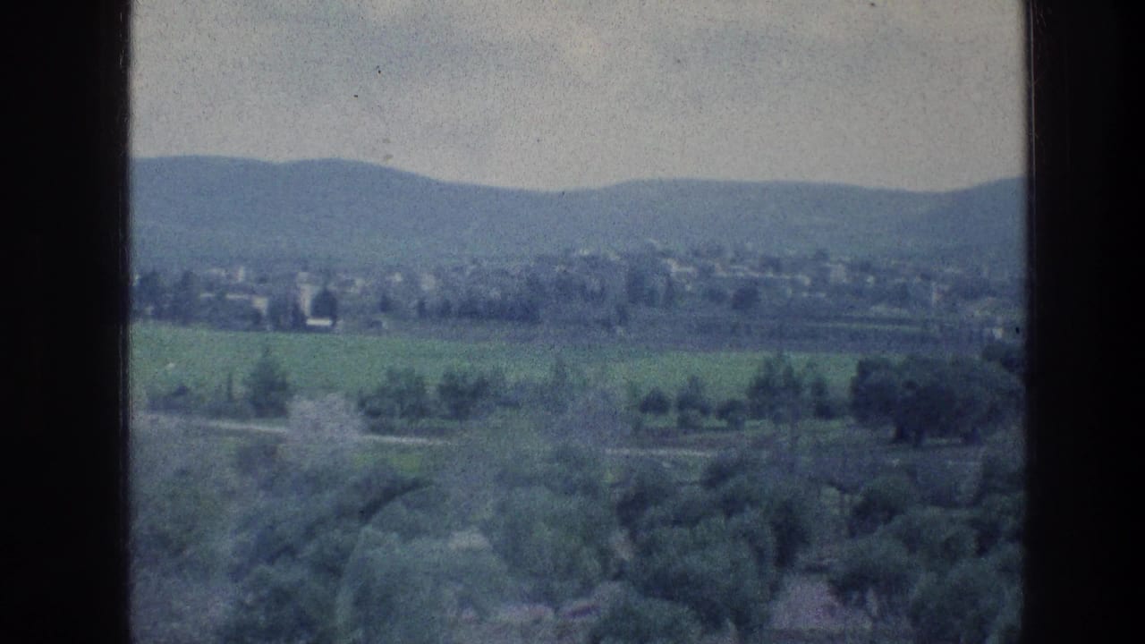 Wide 1976 travel-film view of a rural landscape near the stated Jerusalem reel context, with fields, trees, and hills.