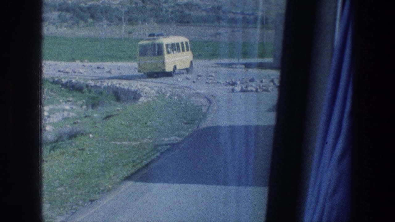 1976 Jerusalem-area home-movie frame showing a small yellow bus on a curving road beside fields and rocky ground.
