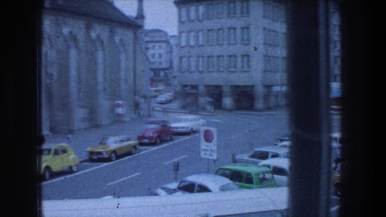 1970s Zurich street corner viewed from indoors, showing parked cars near a large stone building.