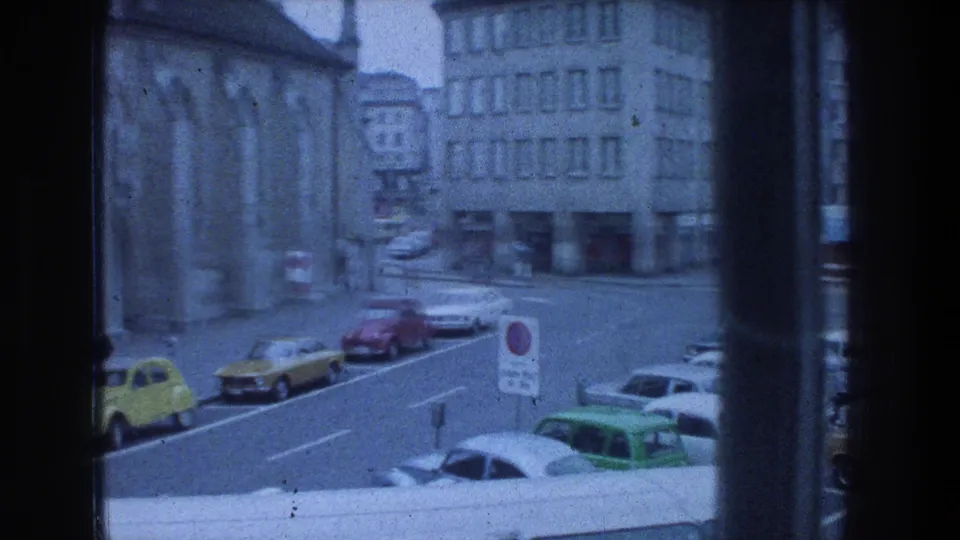 1970s Zurich street corner viewed from indoors, showing parked cars near a large stone building.
