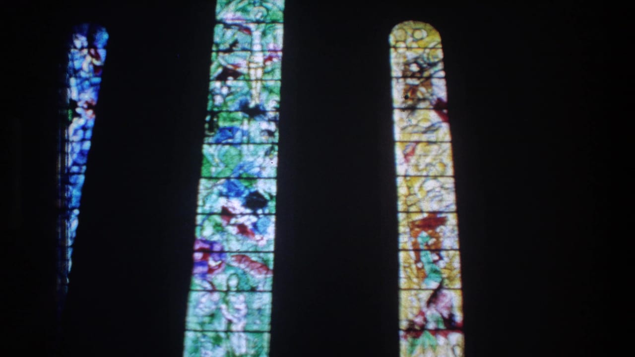 1976 Zurich 8mm frame with narrow arched stained-glass windows in blue, green, and yellow tones.