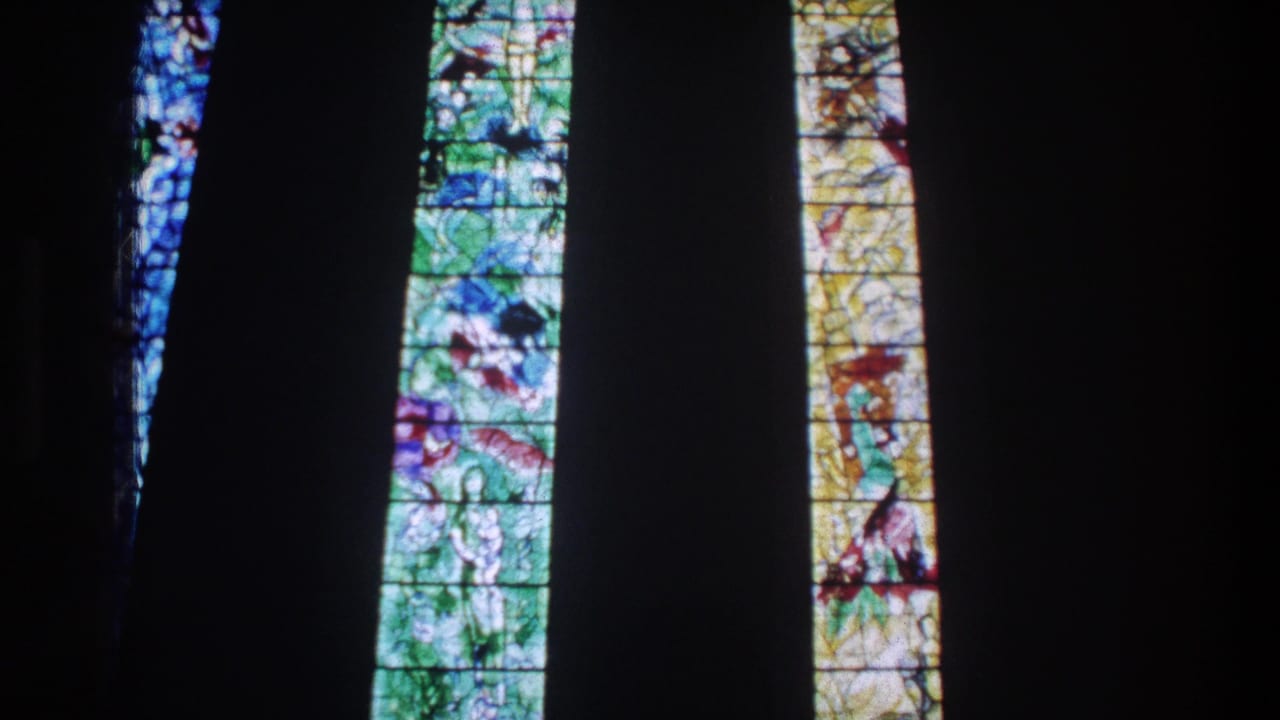 1976 Zurich 8mm frame showing luminous stained-glass panels divided by dark church architecture.