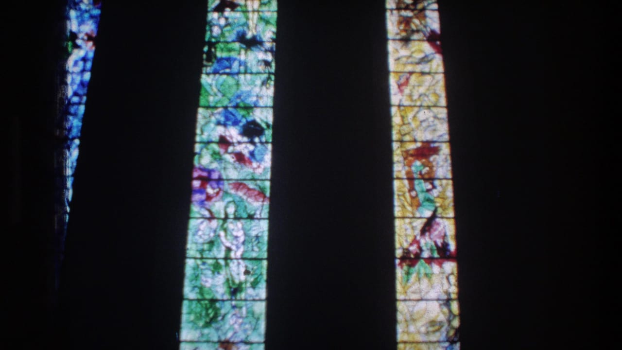 1976 Zurich 8mm frame of bright arched stained-glass windows surrounded by a dark church interior.