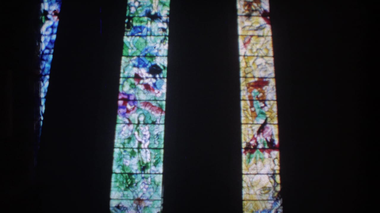 1976 Zurich church interior with narrow stained glass panels lit against deep shadows.