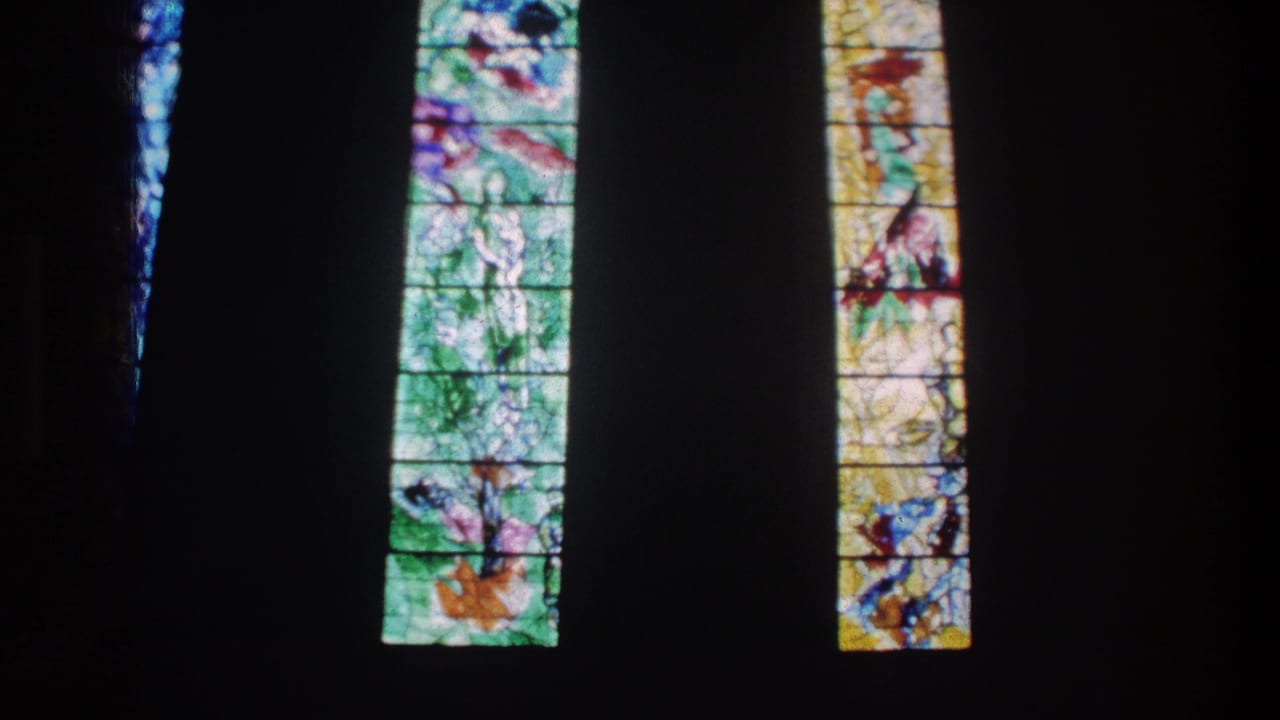 End of the 1976 Zurich pan across narrow stained glass windows inside a dim church interior.