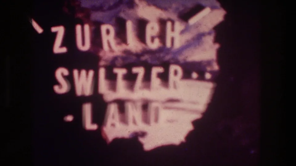 1976 8mm frame showing the Zurich Switzerland title card centered over a pink map silhouette with visible grain and fading.