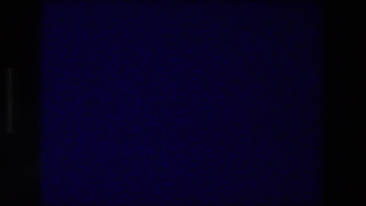 Blue 8mm projection frame near the reel ending, with dark borders, grain, and low-light color shift in the cinema room.