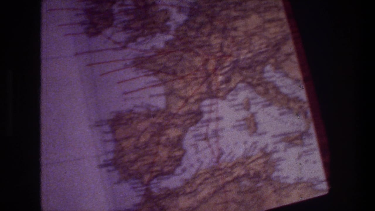 A tilted close-up of the printed map shows Mediterranean-region forms, grid markings, and the red edge of the page within the 8mm frame.