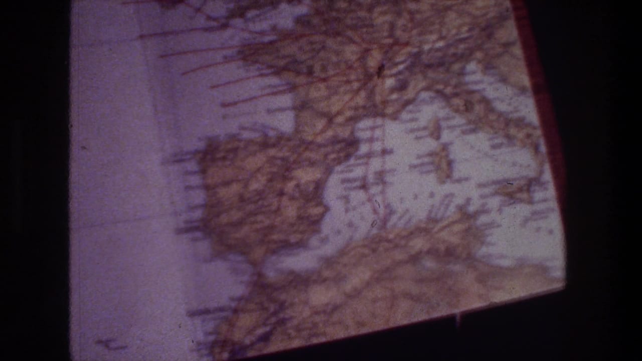 The final frame shows the printed map at an angle, with coastline outlines, grid marks, brown shading, and dark borders from the 8mm scan.