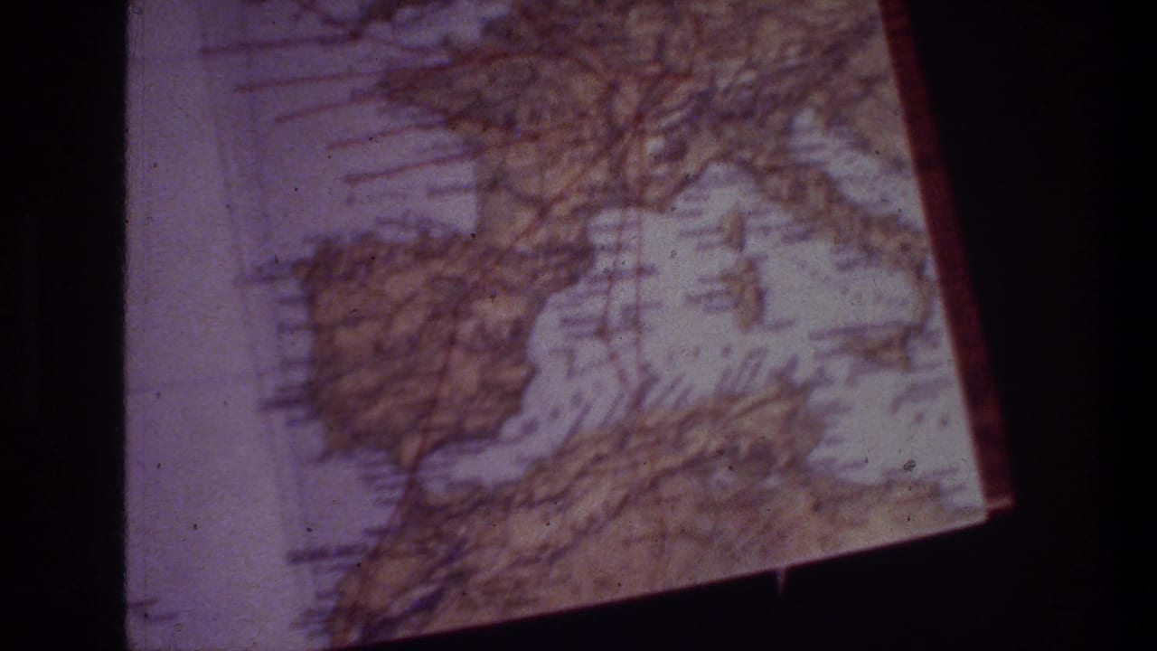 1970s 8mm travel footage frame showing a tilted, worn European map with visible grid lines and purple color shift.