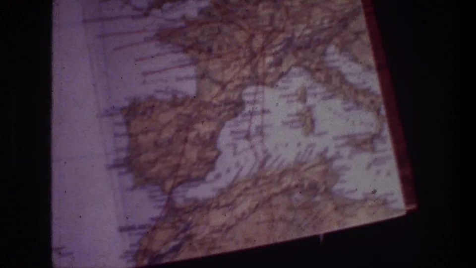 1970s 8mm travel footage frame showing a tilted, worn European map with visible grid lines and purple color shift.