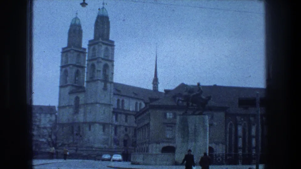 1976 Zurich home-movie view of Grossmunster, an equestrian statue, cobblestones, and distant pedestrians.