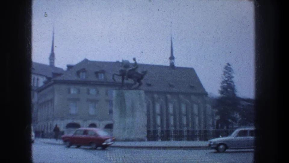1976 Zurich view of an equestrian statue, railings, stone architecture, and passing cars on a cobbled street.
