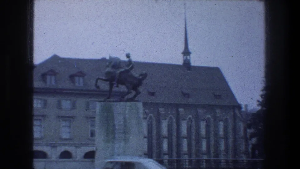 Zurich landmark cutaway showing an equestrian statue, historic stone building, railings, and spire in blue-tinted 8mm footage.