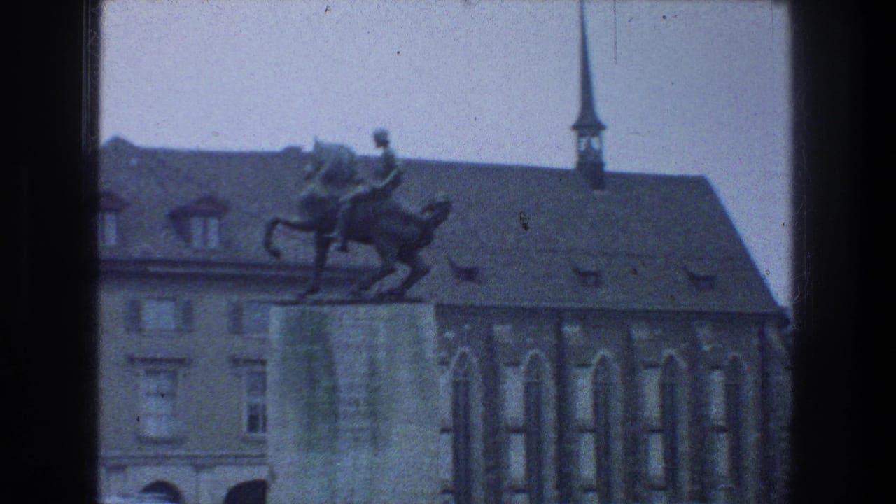 Equestrian statue on a stone pedestal in front of historic buildings and a spire.