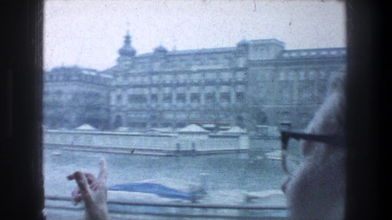 1976 Zurich tour view across water toward multi-story buildings, with a railing and a glasses-wearing passenger partially visible in the foreground.