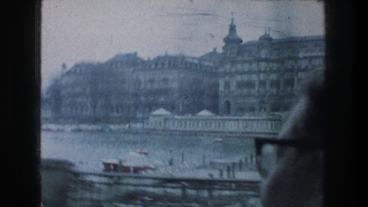 1976 Zurich 8mm frame showing a man in glasses at a train window with riverfront buildings and small boats outside.