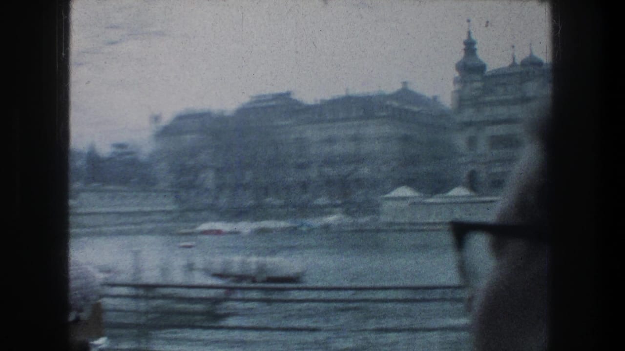 Motion-blurred 8mm view of Zurich riverfront buildings from a train, with the man in glasses partially visible.