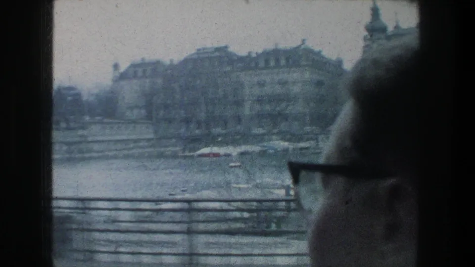 1976 Zurich passenger view across lake water toward waterfront buildings, partly obscured by a person wearing glasses.