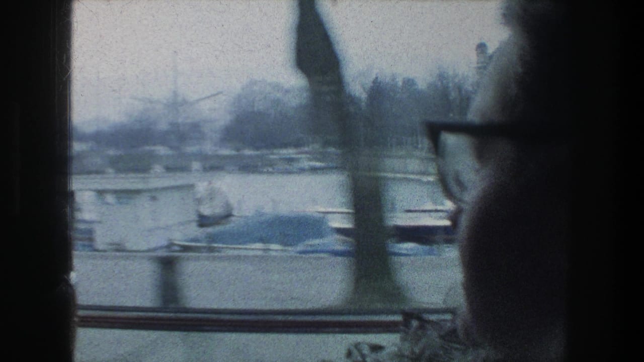 In Zurich, Switzerland, a woman in glasses sits by a moving vehicle window as boats and bare trees pass outside in 1976 home-movie footage.