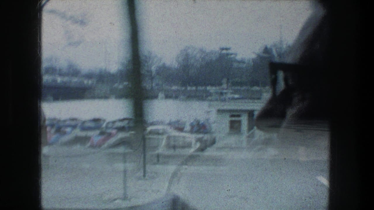 A soft, blurred 8mm view through the vehicle window shows lakeside boats, trees, and street fixtures in Zurich.