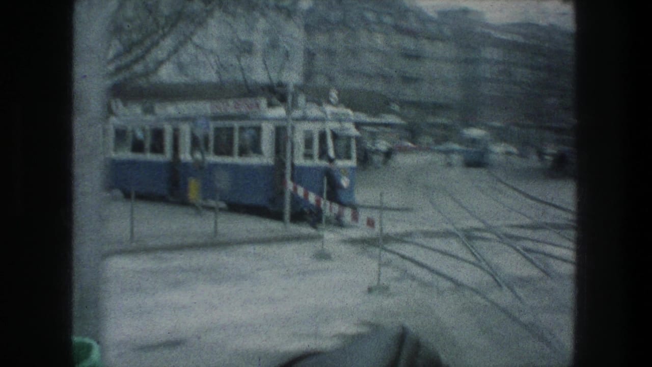 1976 Zurich street view from a moving vehicle, showing a blue-and-white tram, streetcar tracks, barriers, and city facades.
