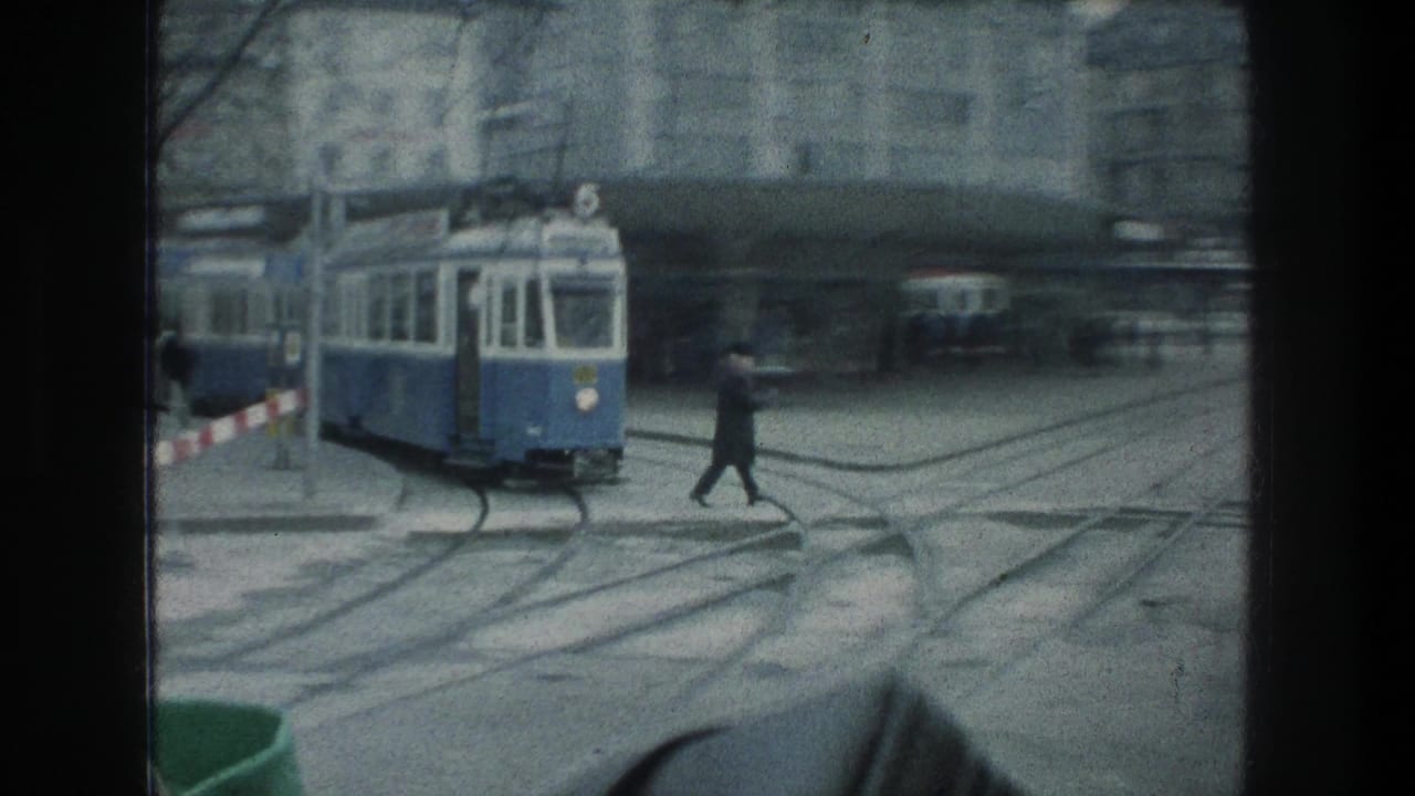 A pedestrian crosses the tracks near a blue-and-white tram in 1976 Zurich, with overhead wires and city buildings behind.