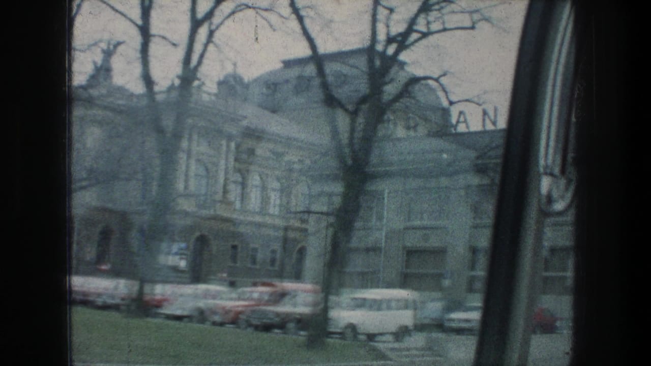 1976 Zurich street pass showing a masonry building, arched doorway, parked cars, bare tree branches, and partial rooftop sign letters.