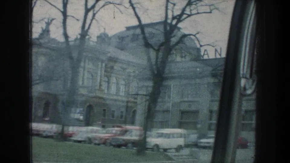 1976 Zurich street pass showing a masonry building, arched doorway, parked cars, bare tree branches, and partial rooftop sign letters.
