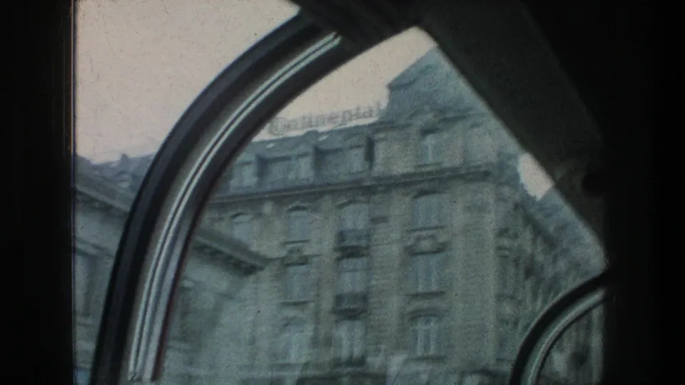 Zurich building facade from 1976 8mm footage, partly obscured by dark curved window frames as the camera passes.