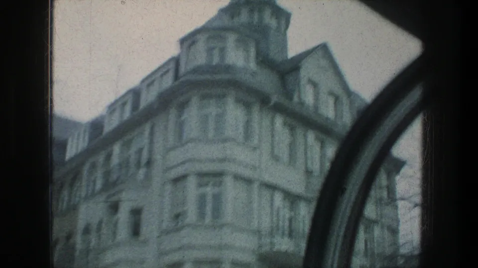A rounded corner facade in Zurich appears in soft 1976 8mm color, framed by a dark curved window edge during travel.
