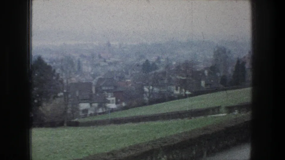 1976 Zurich home-movie frame showing a green hillside, suburban houses, bare trees, and distant city haze.