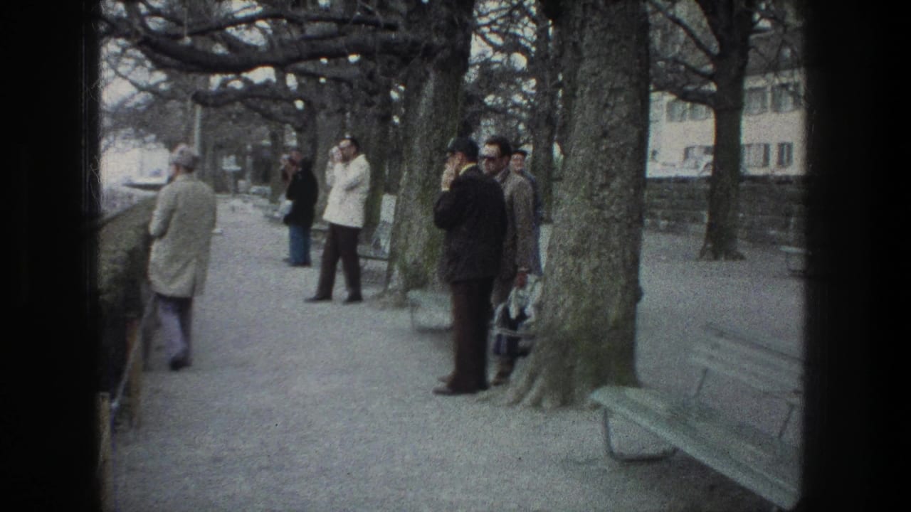 1976 Zurich park-path scene with several men in coats standing near bare trees, benches, and a low wall.