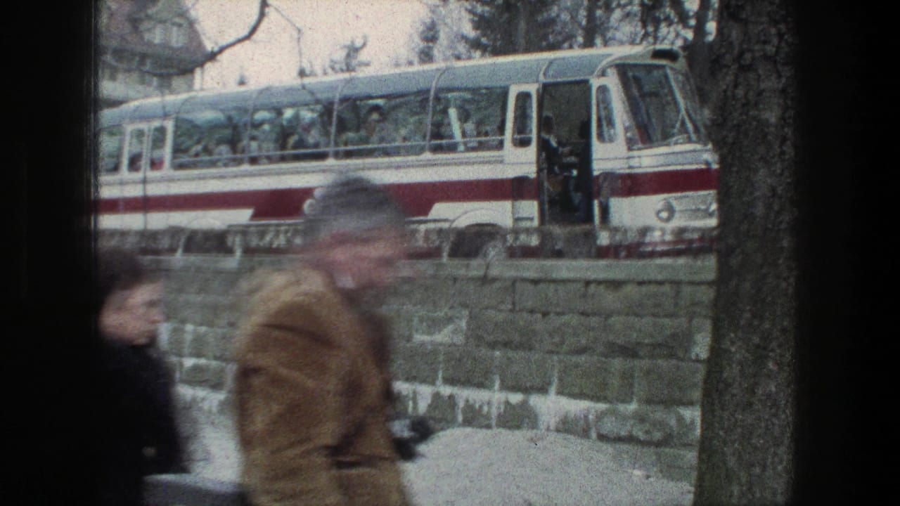 A red-and-white coach bus with passengers or boarding figures appears beyond a stone wall in Zurich, while blurred pedestrians pass in the foreground.