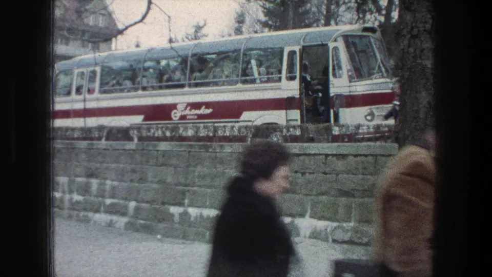 1976 Zurich street view with a red-and-white bus stopped behind a stone wall and pedestrians partly obscuring the camera.