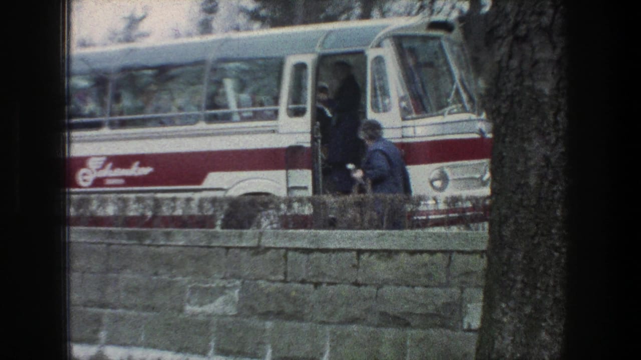 1976 Zurich bus stop scene showing a person approaching the open door of a red-and-white bus near a stone wall.