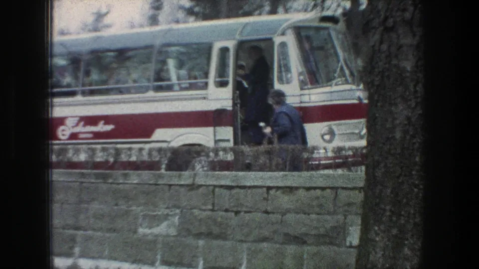 1976 Zurich bus stop scene showing a person approaching the open door of a red-and-white bus near a stone wall.