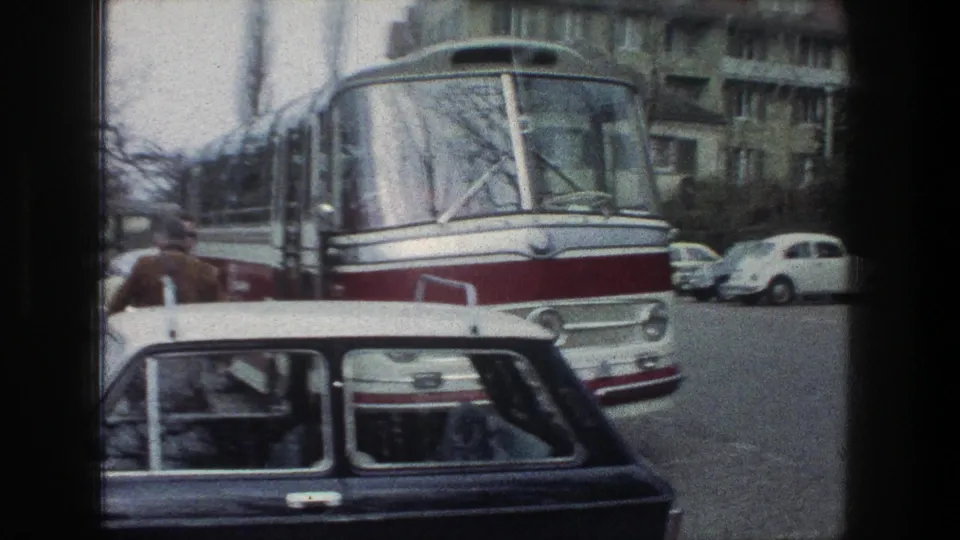 1976 Zurich street frame with the front of a red-and-white bus, parked compact cars, pedestrians, and residential buildings.