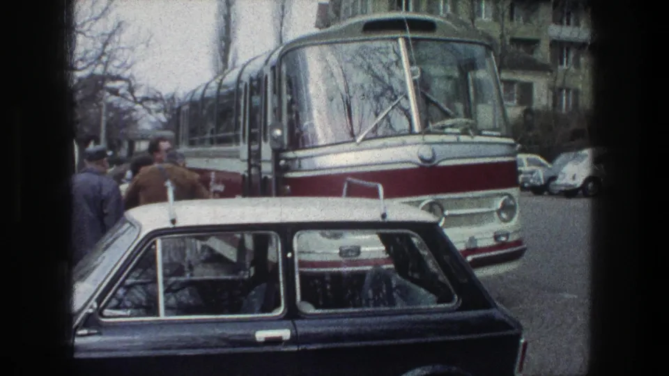 1976 Zurich street view of a red-and-white bus facing the camera as pedestrians stand near the curb and a dark car is parked in front.
